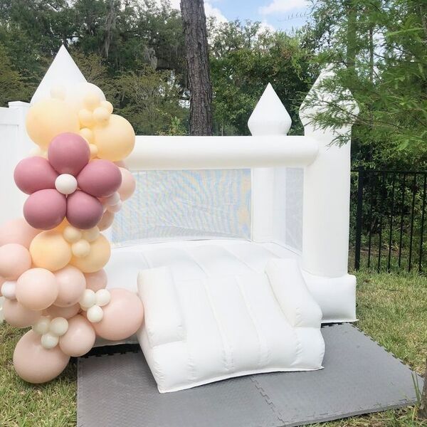 Balloon-decorated outdoor bounce house with pastel flowers and white cushions on a backyard patio