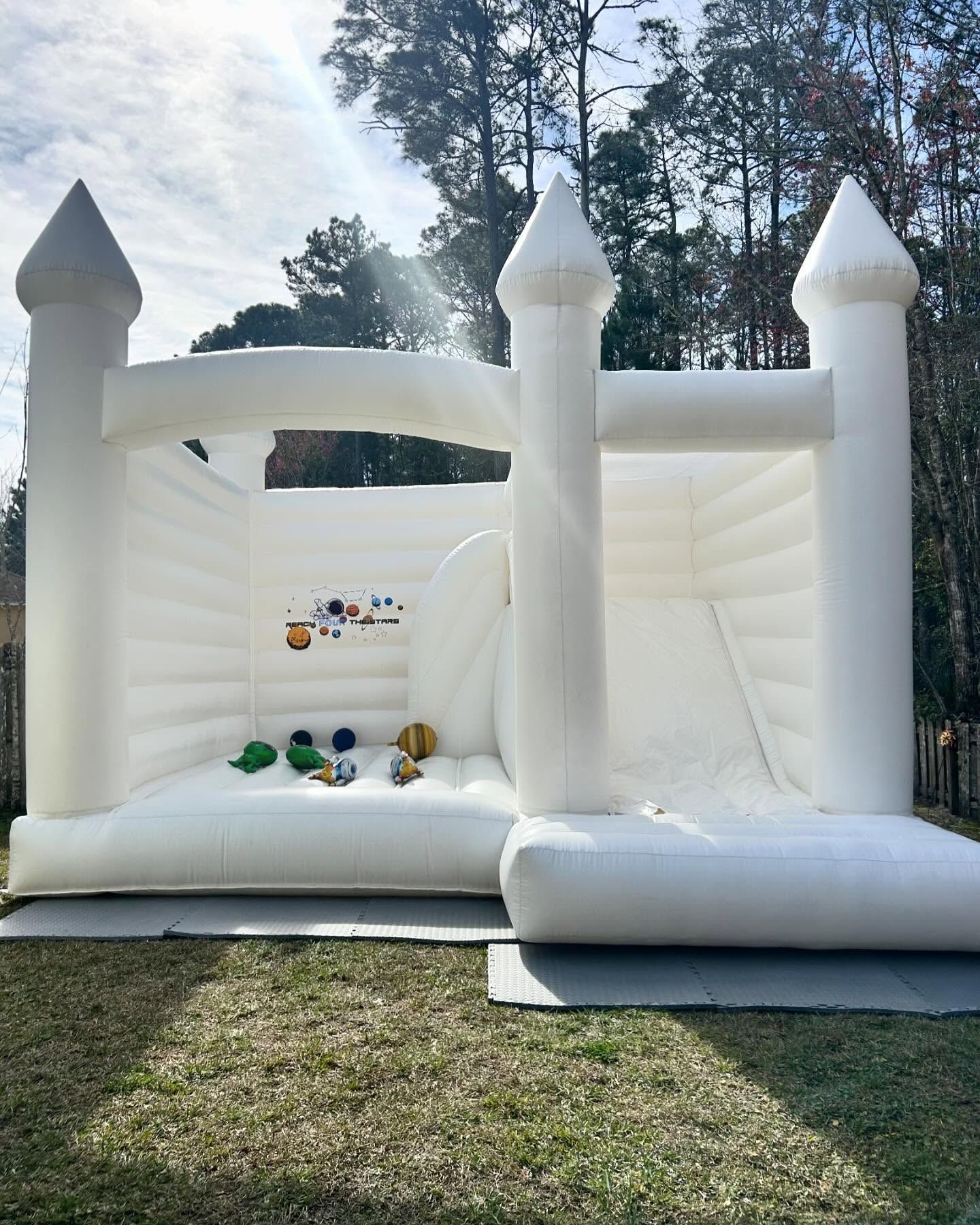 White inflatable castle bounce house on grass with colorful balls, outdoors among trees