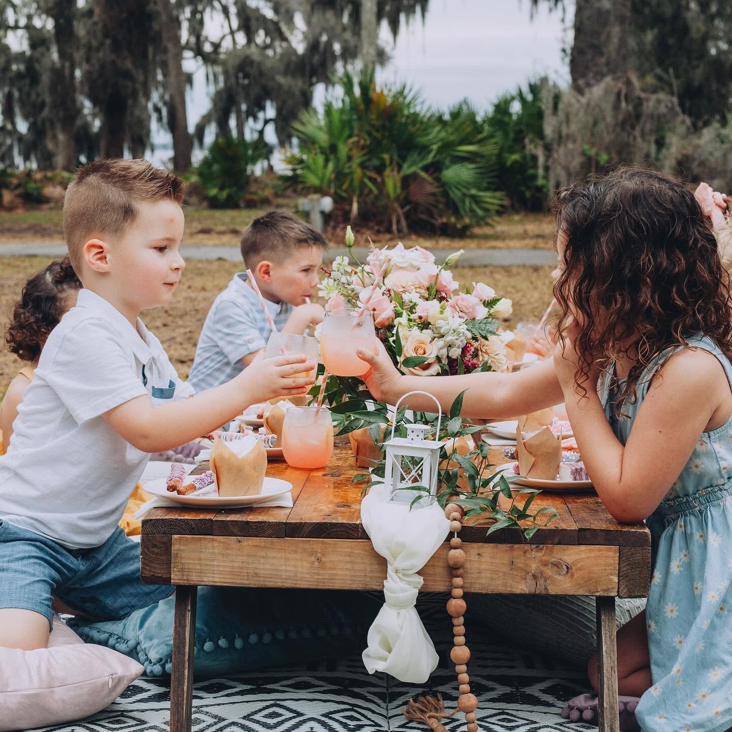 Children sharing drinks at a picnic table with flowers and lanterns outdoors