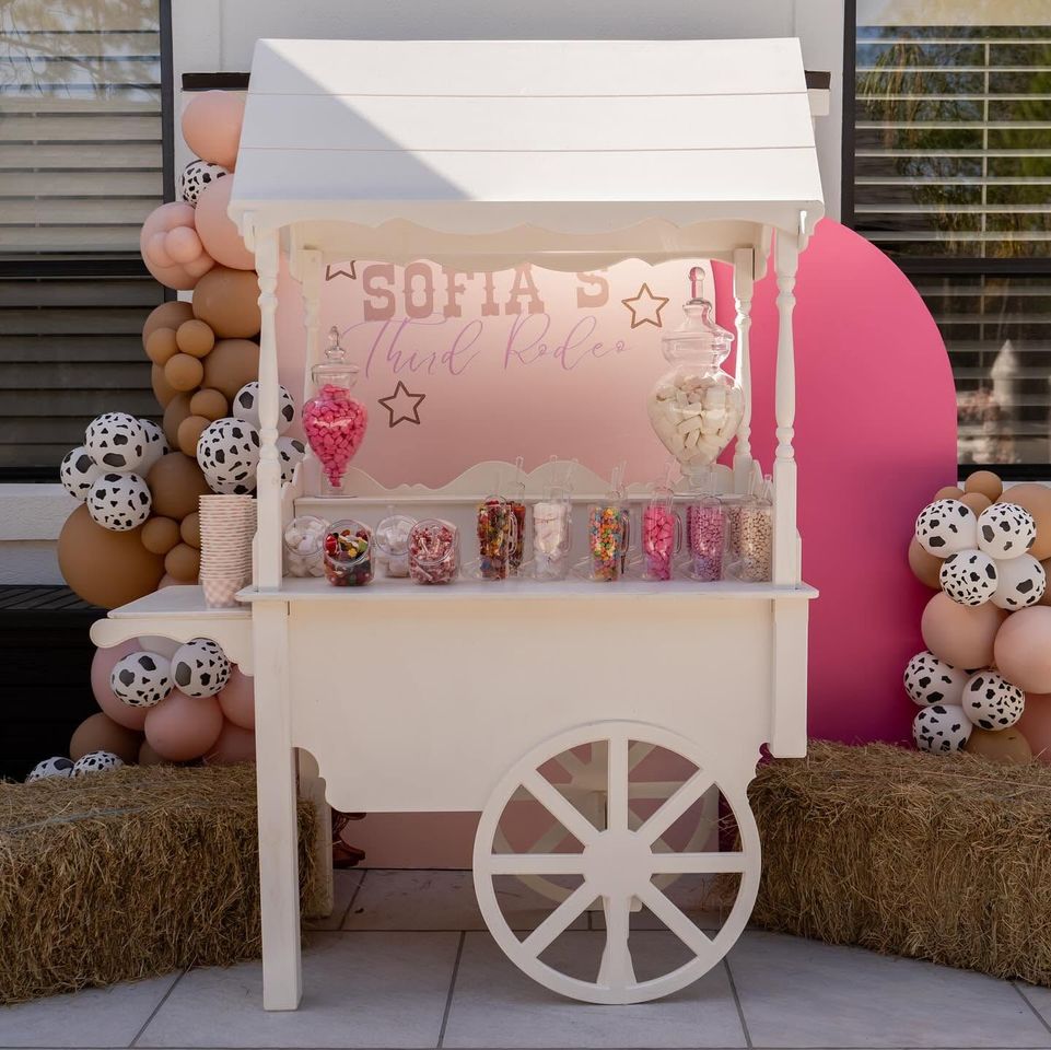 Pink and white dessert cart with Sofia sign, candy display, and balloon decorations outdoors