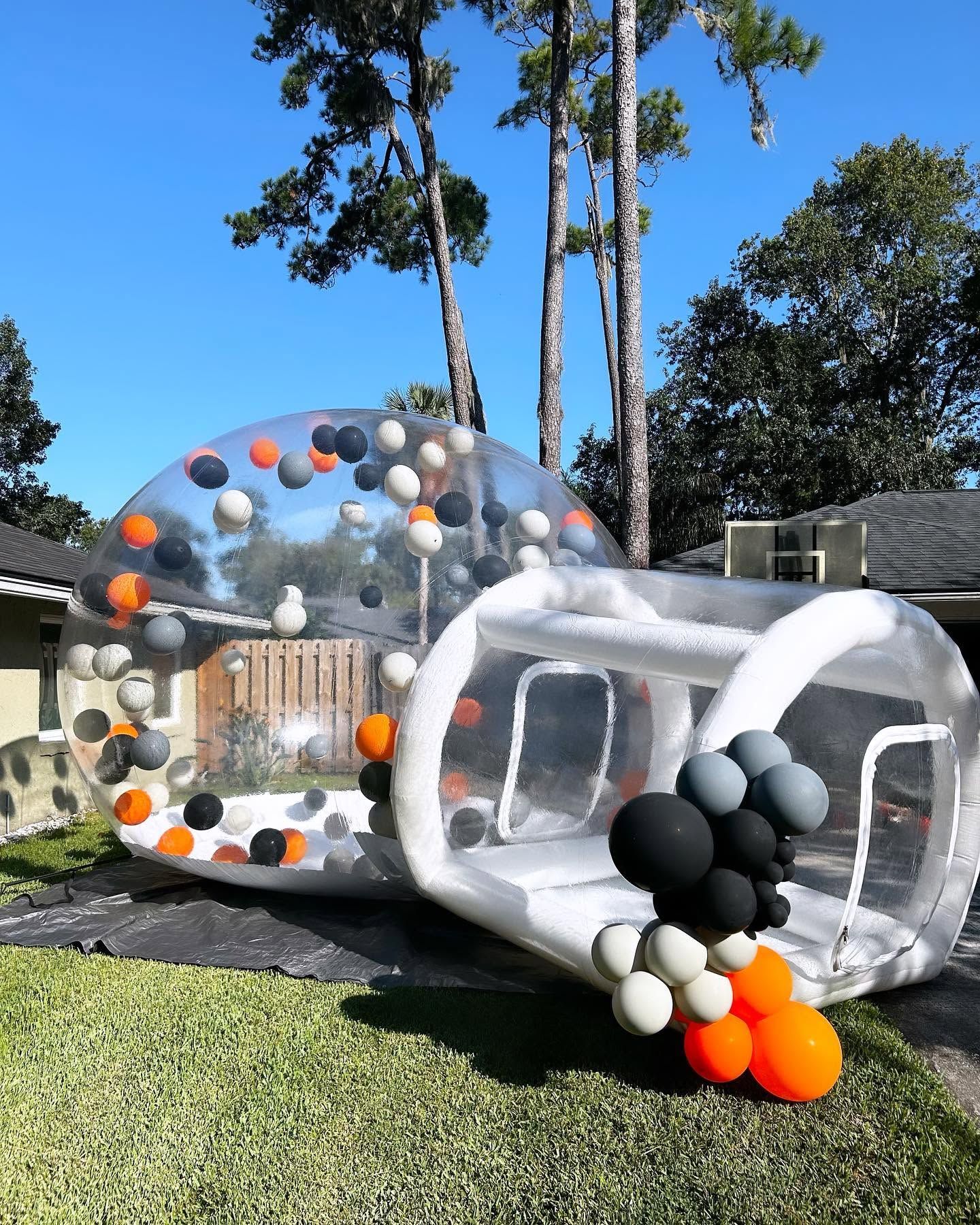 Transparent inflatable sculpture with black, white, orange, and gray spheres on a grassy outdoor lawn