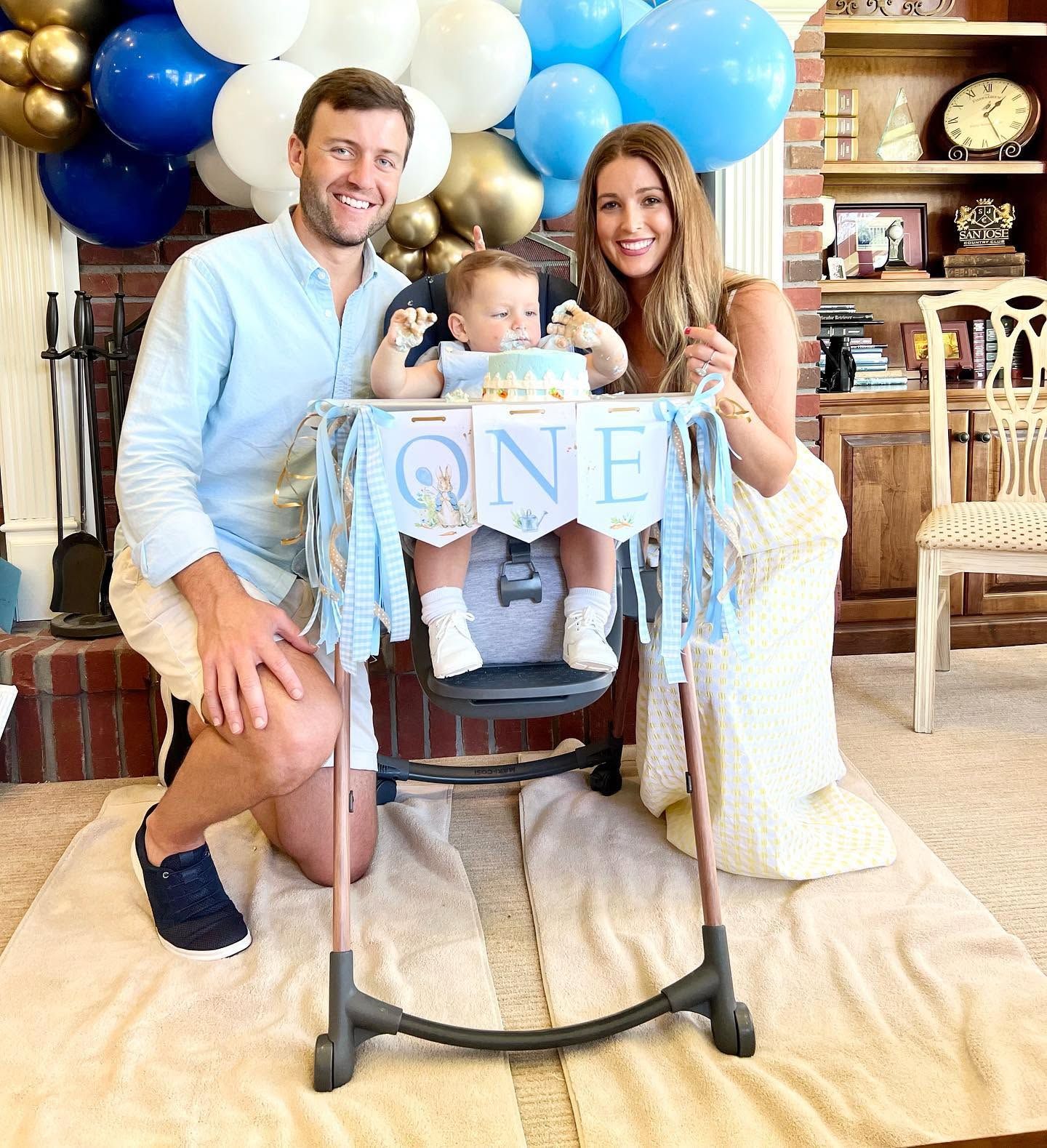 Family celebrating a baby’s first birthday with balloons and a ONE highchair banner