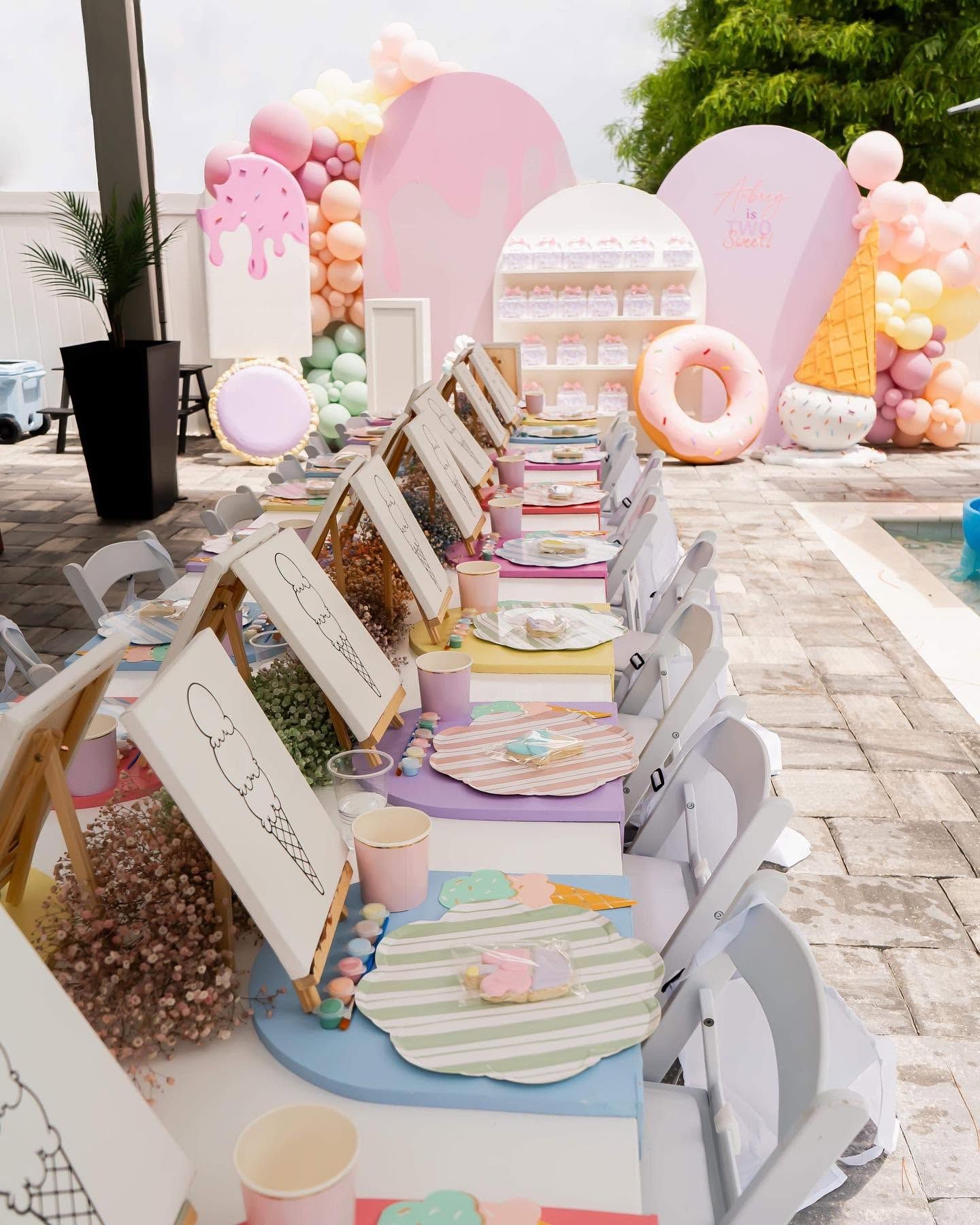 Pastel outdoor dessert table with cake, donuts, and party favors