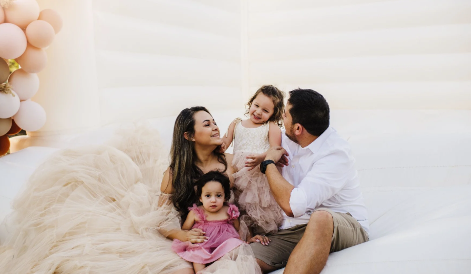 Family sitting on a bed with balloons, smiling and playing with two young children