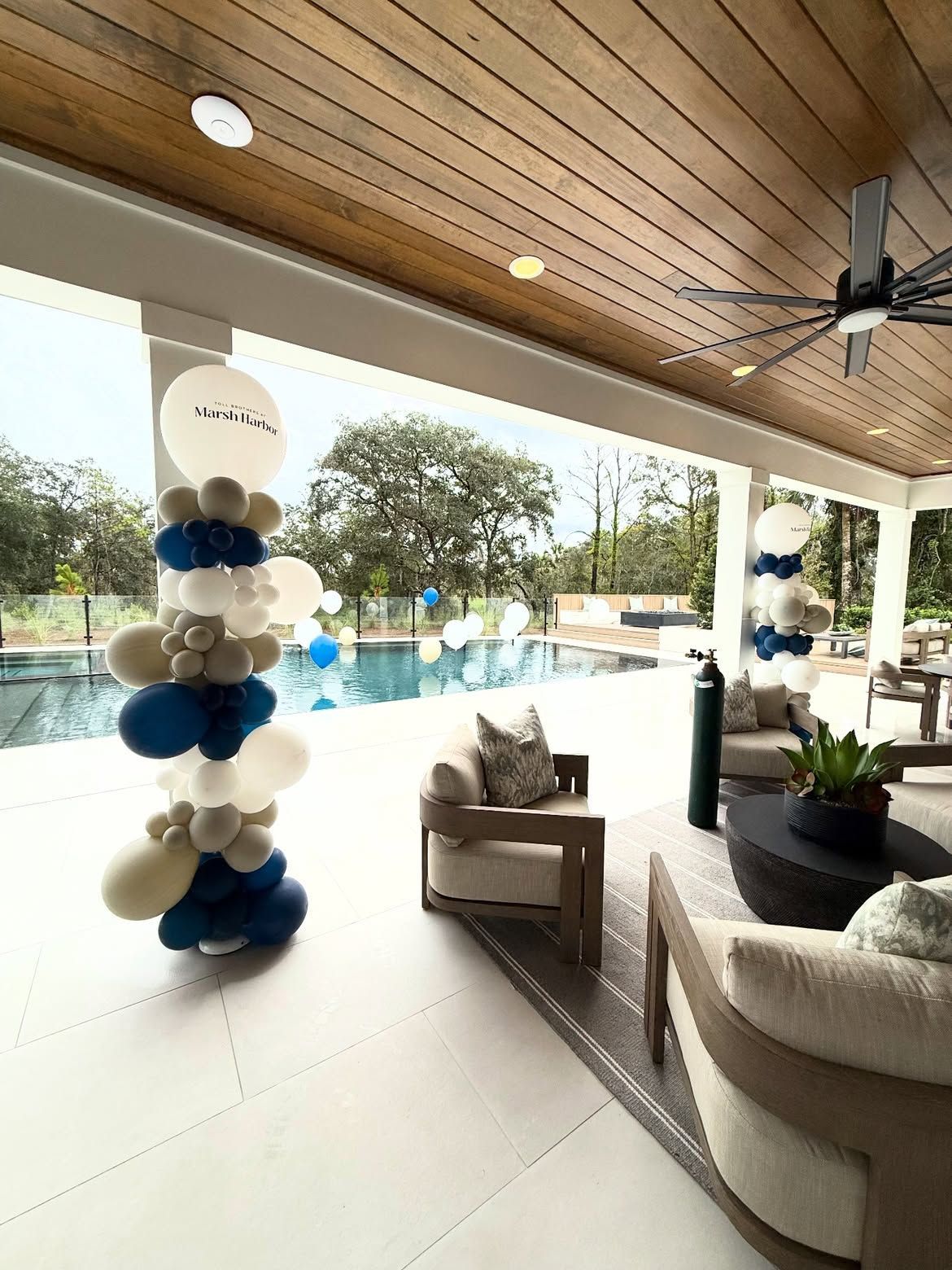 Covered patio with balloon column, seating, pool, and palm trees in the background