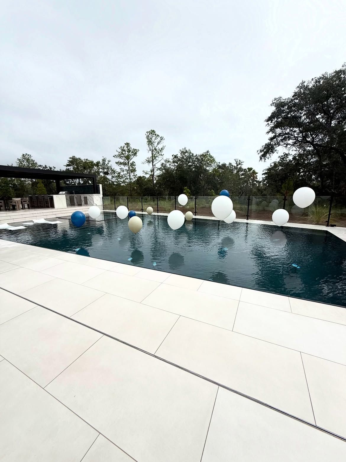 Modern outdoor pool with white balloons along the edge and white stone decking under an overcast sky