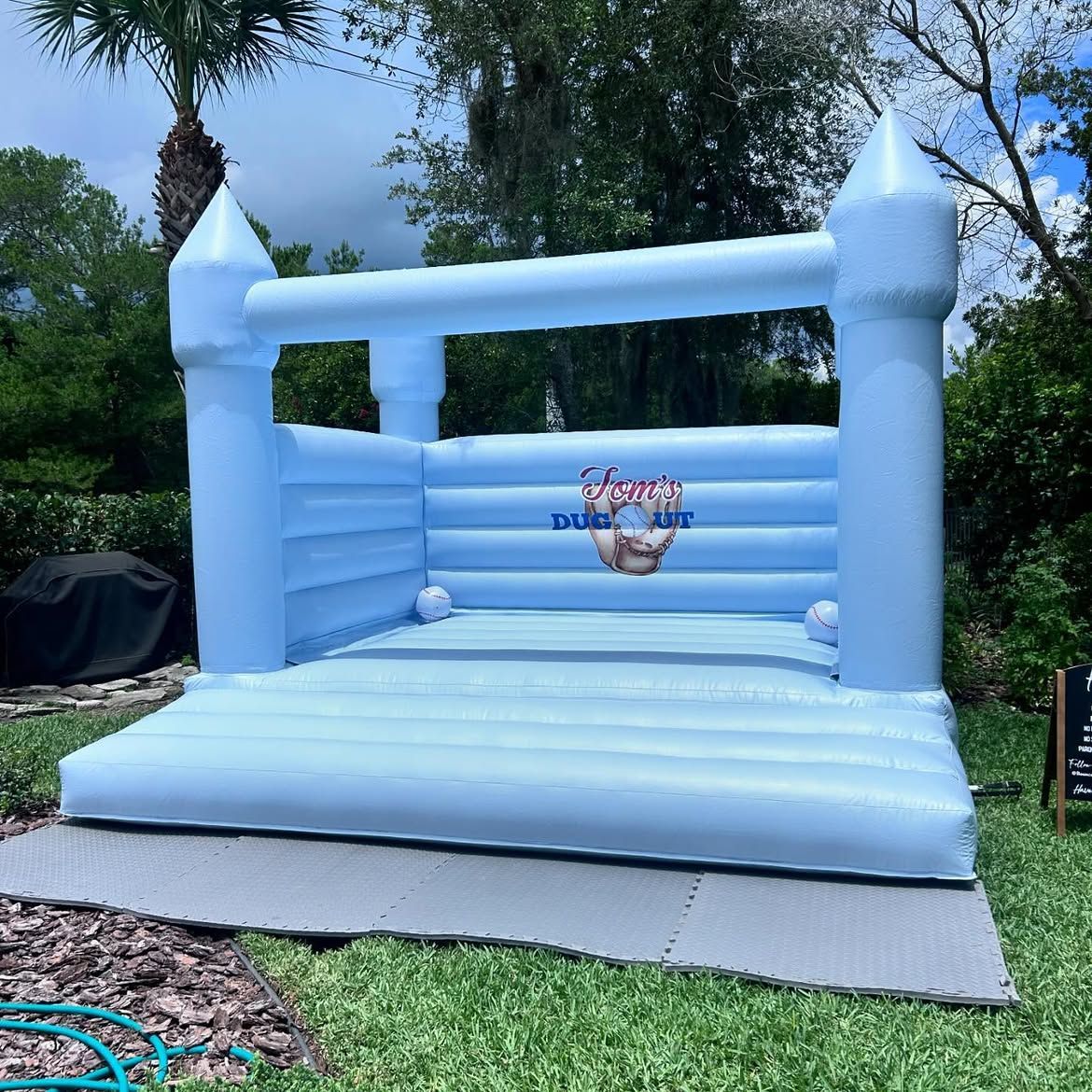 Light blue inflatable bouncy castle in a grassy backyard with trees and a cloudy sky
