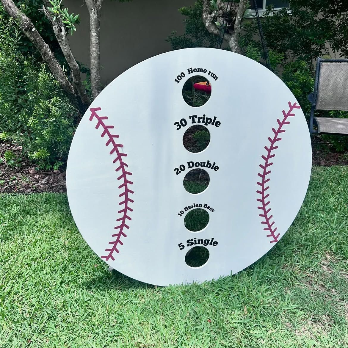 White baseball target board with three numbered holes, red seam graphics, on grass outdoors