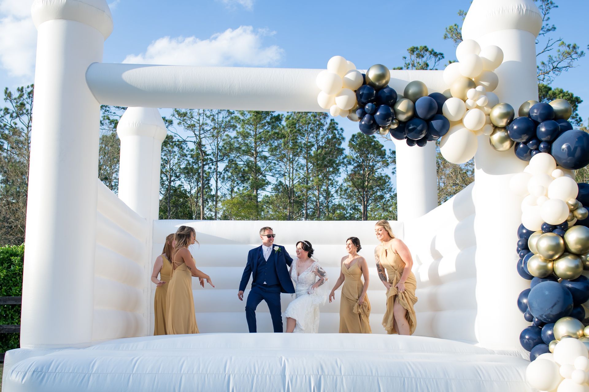 Bride and groom on an outdoor white inflatable stage with navy and gold balloon arch