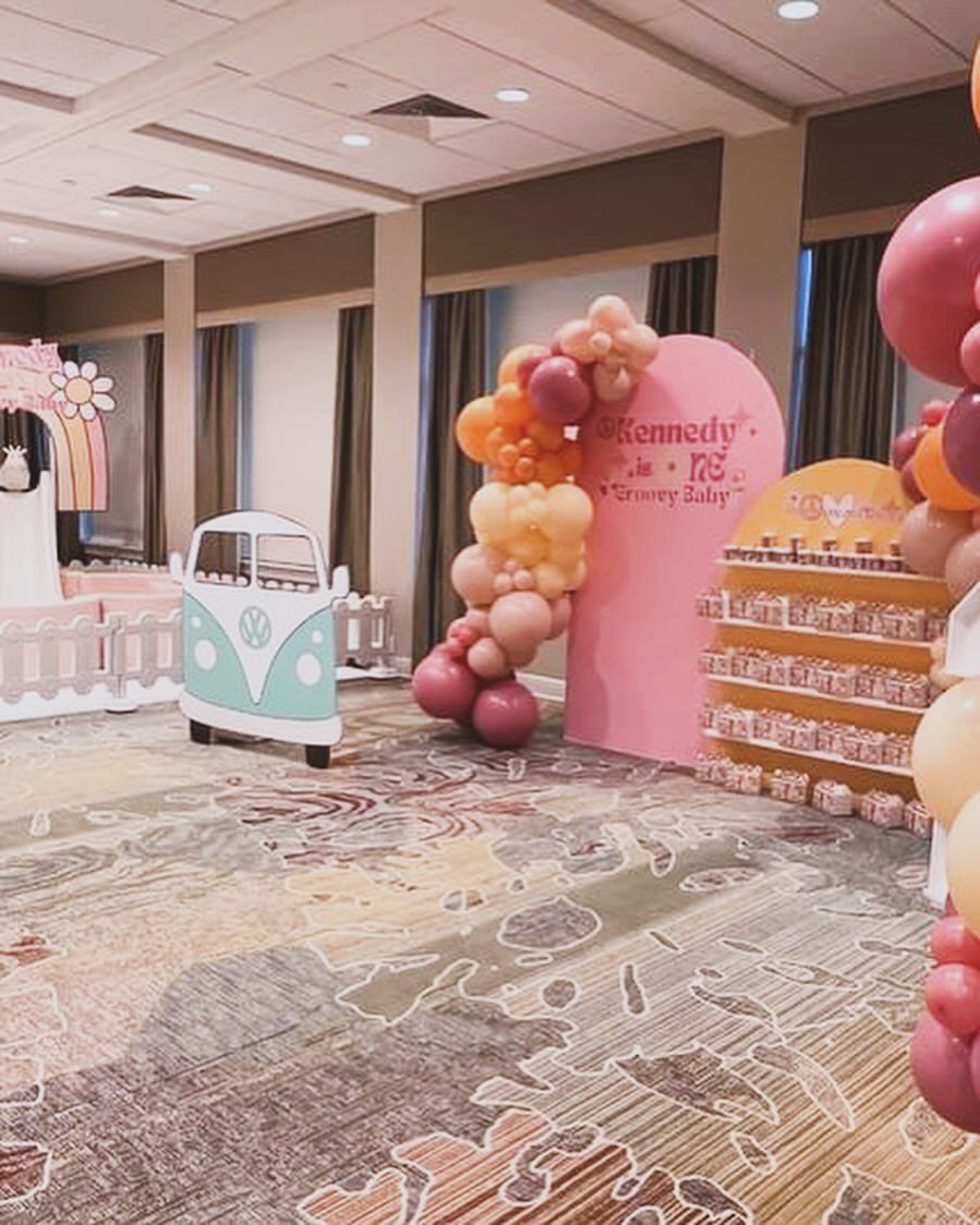 Pastel birthday party setup with balloon arches, pink backdrop, and dessert tables in a hotel ballroom