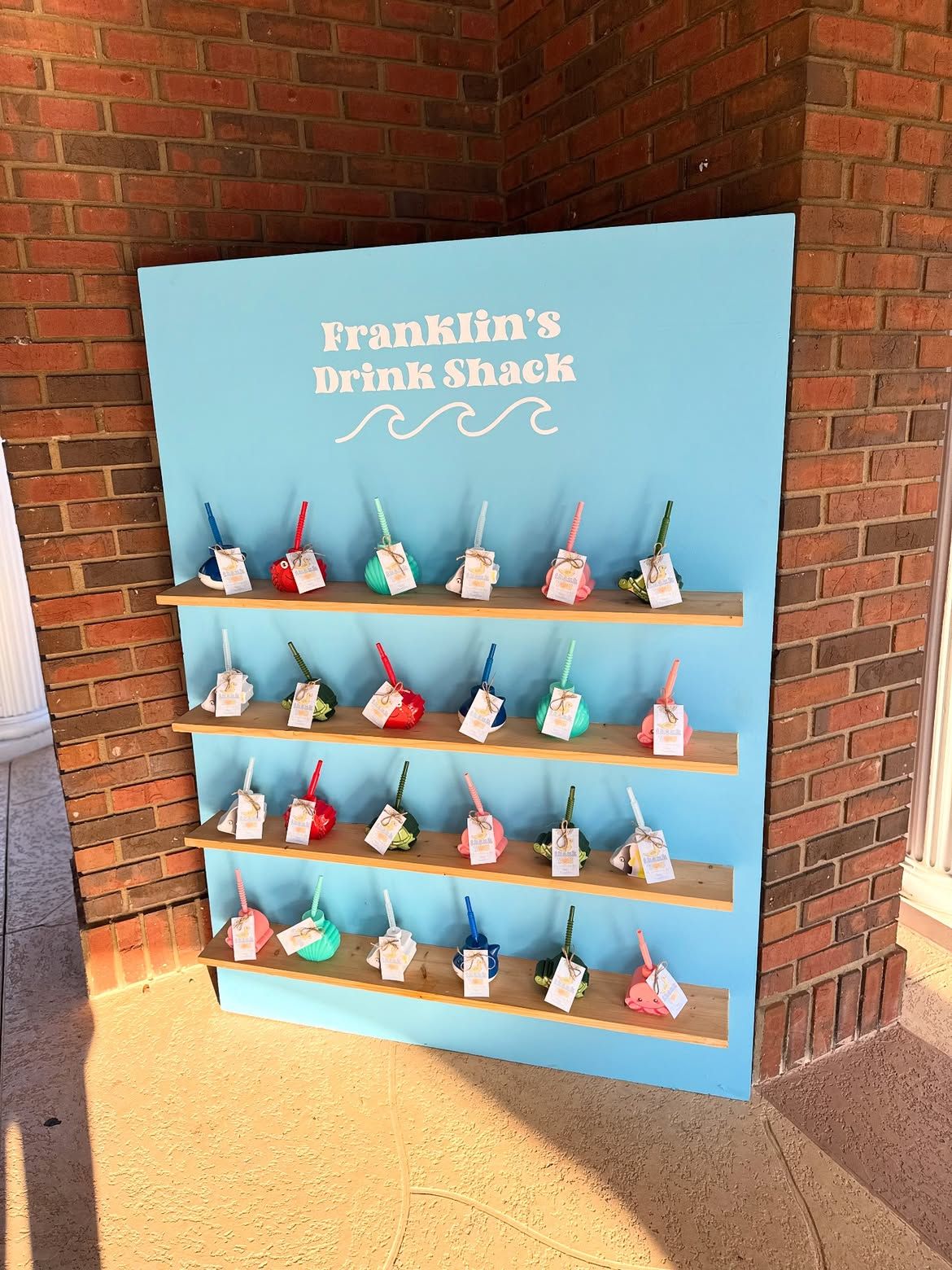 Franklin’s Drink Shack menu display with colorful bottled drinks against a blue sign and brick wall