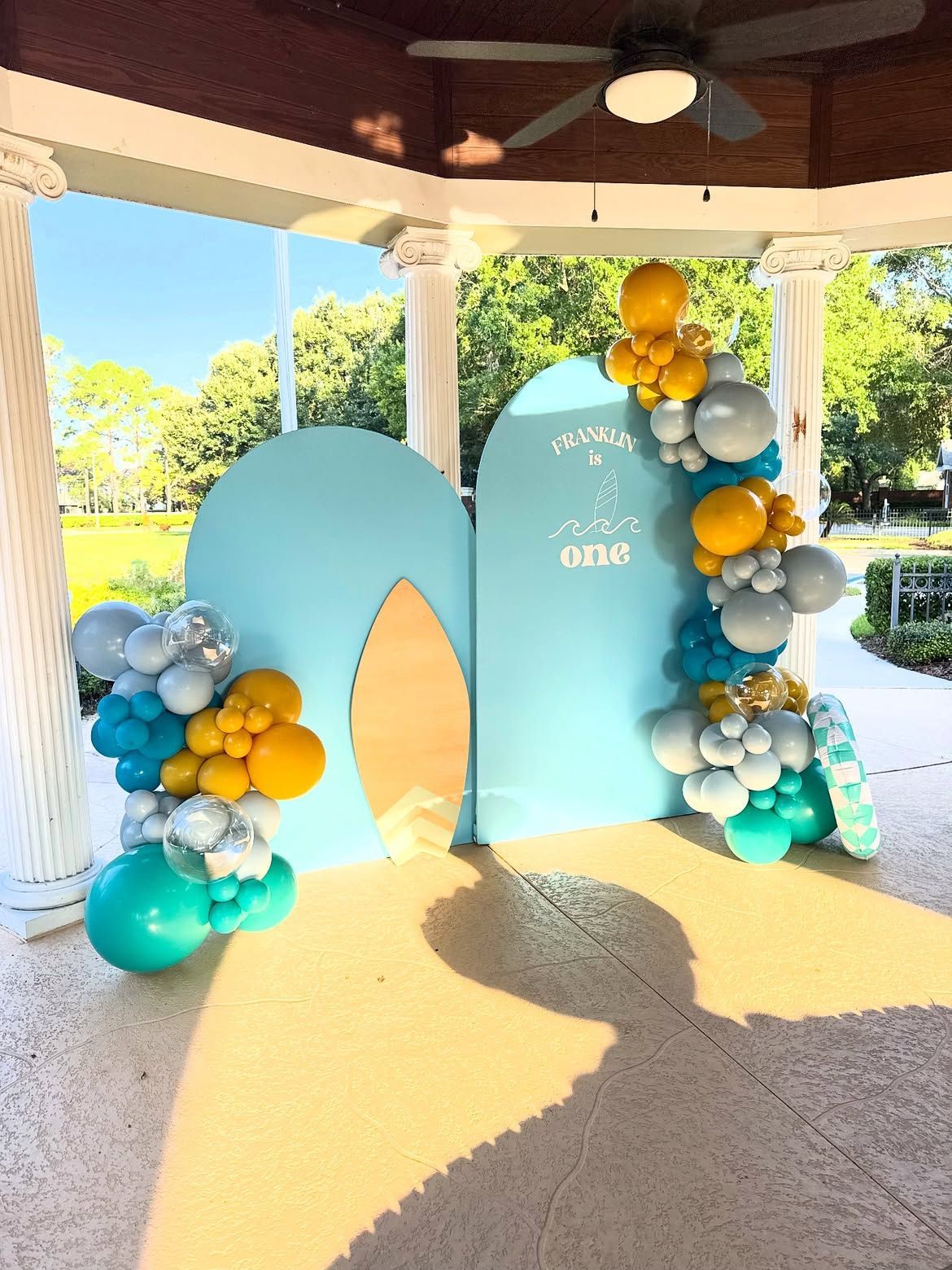 Blue-and-gold balloon arch framing a sign at an outdoor party pavilion
