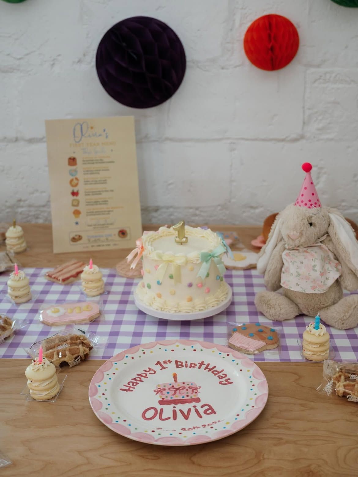 Birthday dessert table with cake, cupcakes, bunny plush, and a plate labeled “Olivia”