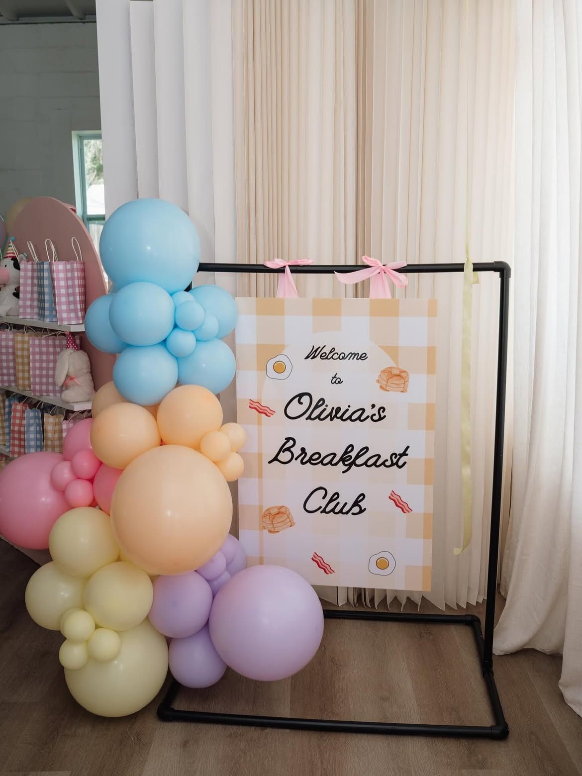 Pastel balloon arch beside a black frame sign for Olivia’s Breakfast Club event