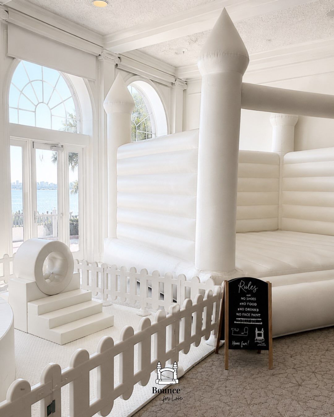 White inflatable bounce house in a bright room with arched windows and a small chalkboard sign.
