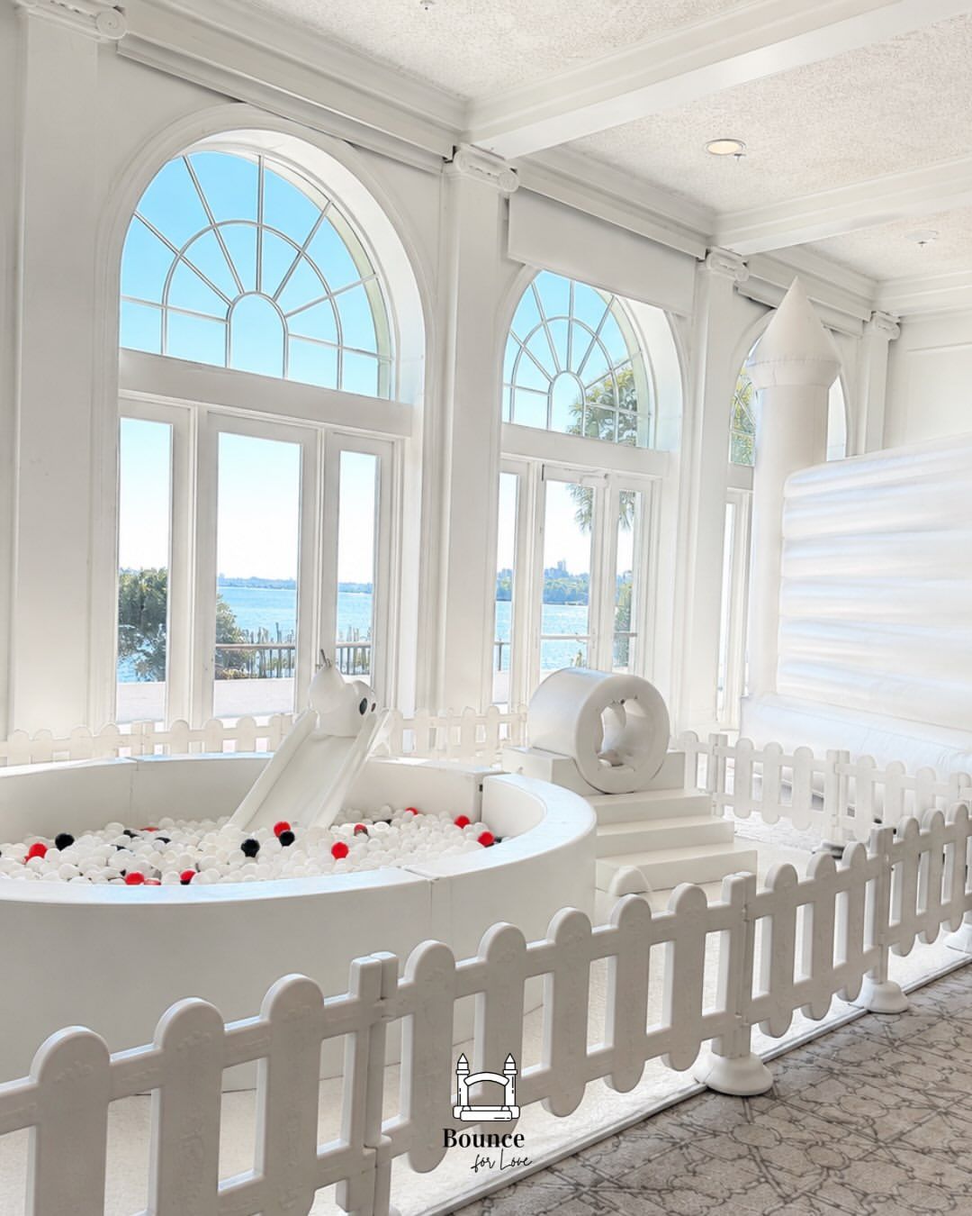Bright white bathroom with a freestanding tub, arched windows, and a small picket fence border