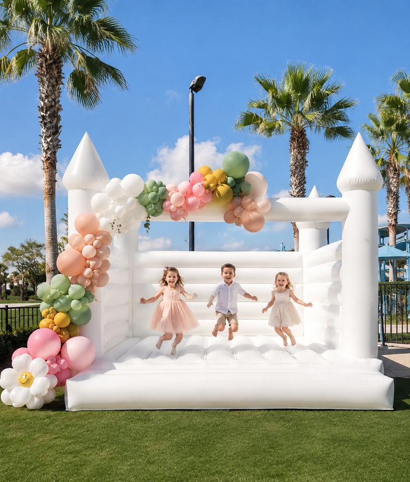 White inflatable bounce house with pastel balloon garland outdoors under cloudy sky.