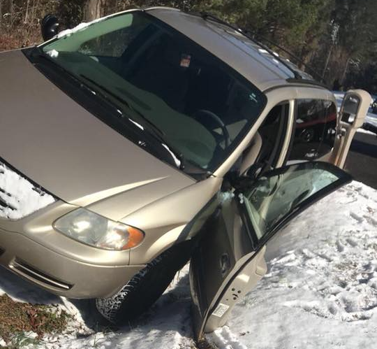 Gold minivan stuck in a snowy ditch with the driver’s side door open