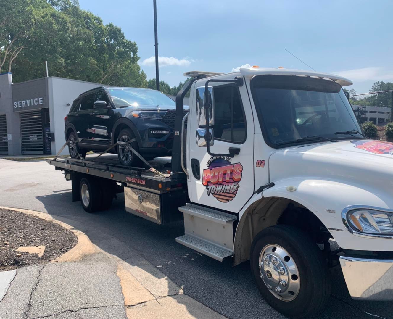 Tow truck carrying a black SUV on a sunny roadside