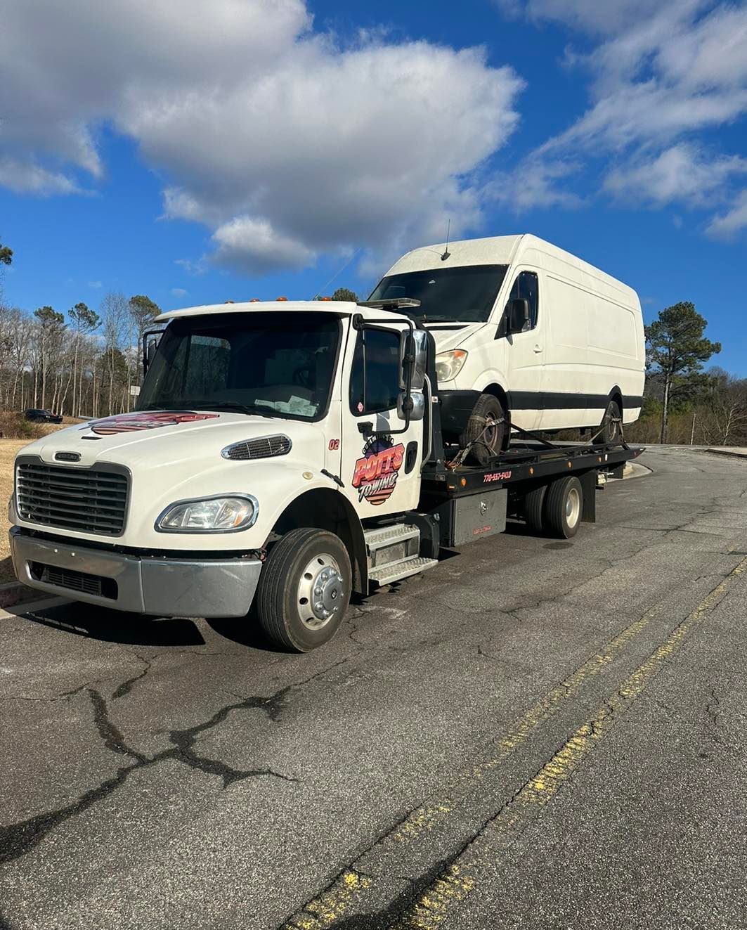White flatbed truck carrying a white cargo van on a road under a blue, cloudy sky.