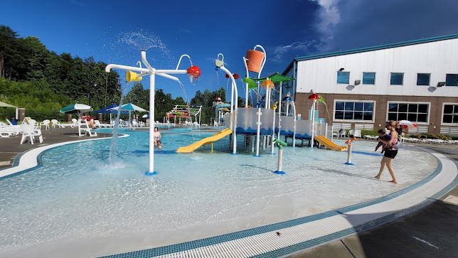 Children playing in a splash pad with water jets and colorful playground structures under a blue sky