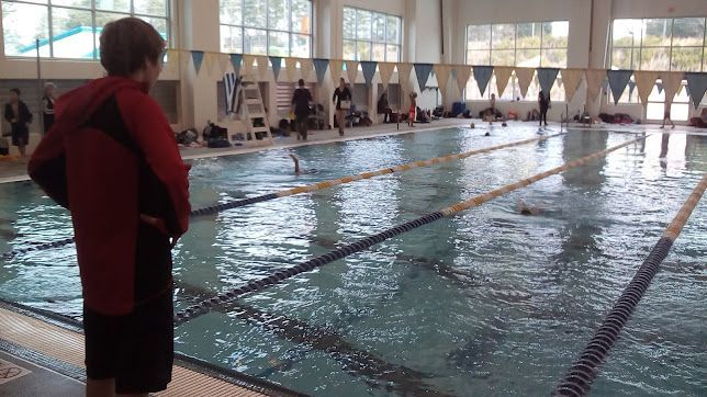 Indoor swimming pool with lanes, a swimmer in the water, and a person standing at the poolside.