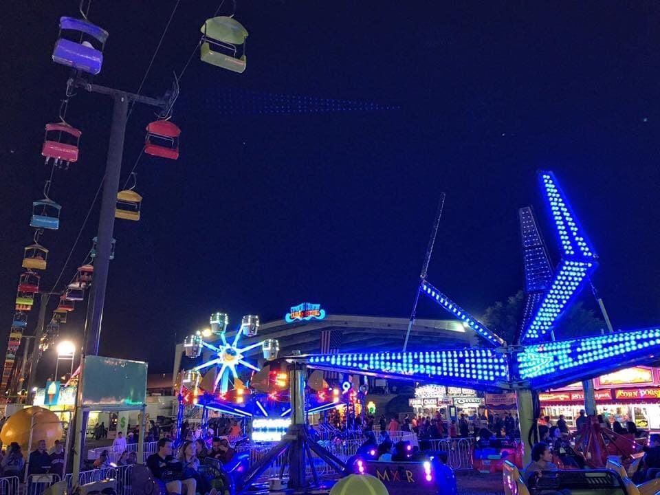 Nighttime fair with colorful lights, rides, and crowds under a dark sky
