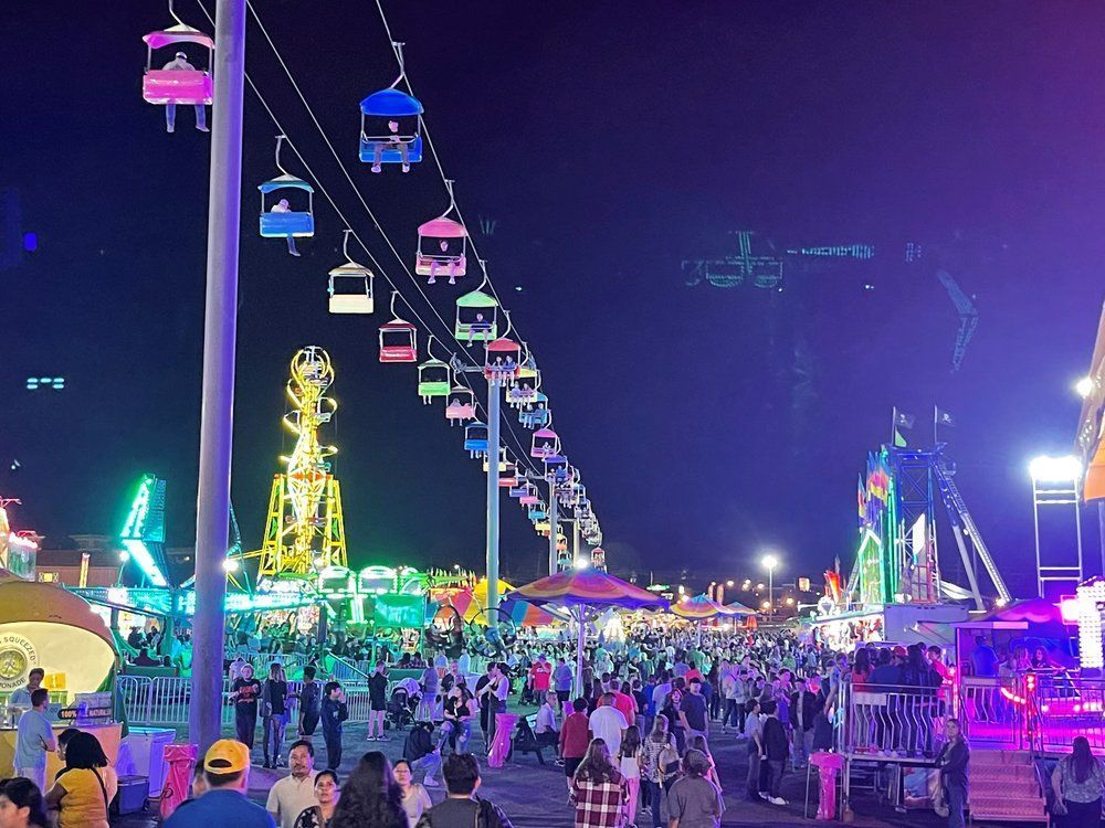 Night fair with colorful Ferris wheel gondolas, bright lights, and crowds walking along a lively midway.