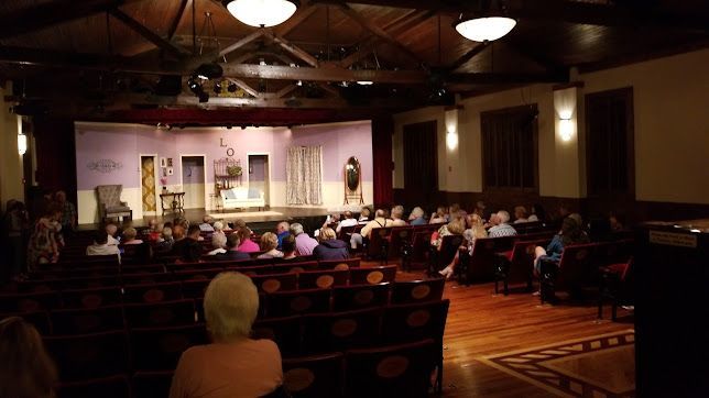 Audience watching a theater stage with performers under warm lights in a small auditorium
