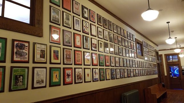 Framed art and photos line a warmly lit hallway with wood paneling and hanging pendant lights.
