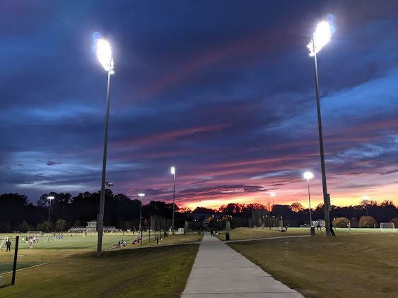 Pathway at dusk in a park, with tall lit lampposts and a colorful sunset sky