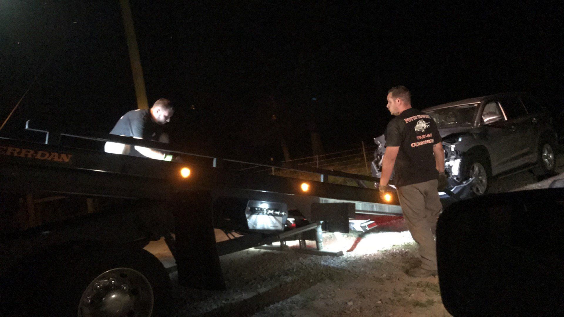 Nighttime roadside towing of a car loaded on a tow truck, with two workers visible.