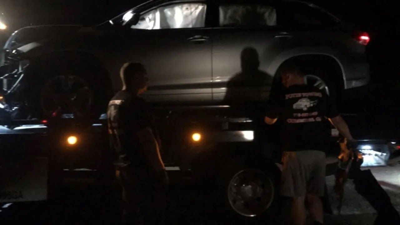 Wrecked red car and white sedan loaded on a tow truck after a crash on a wet roadside