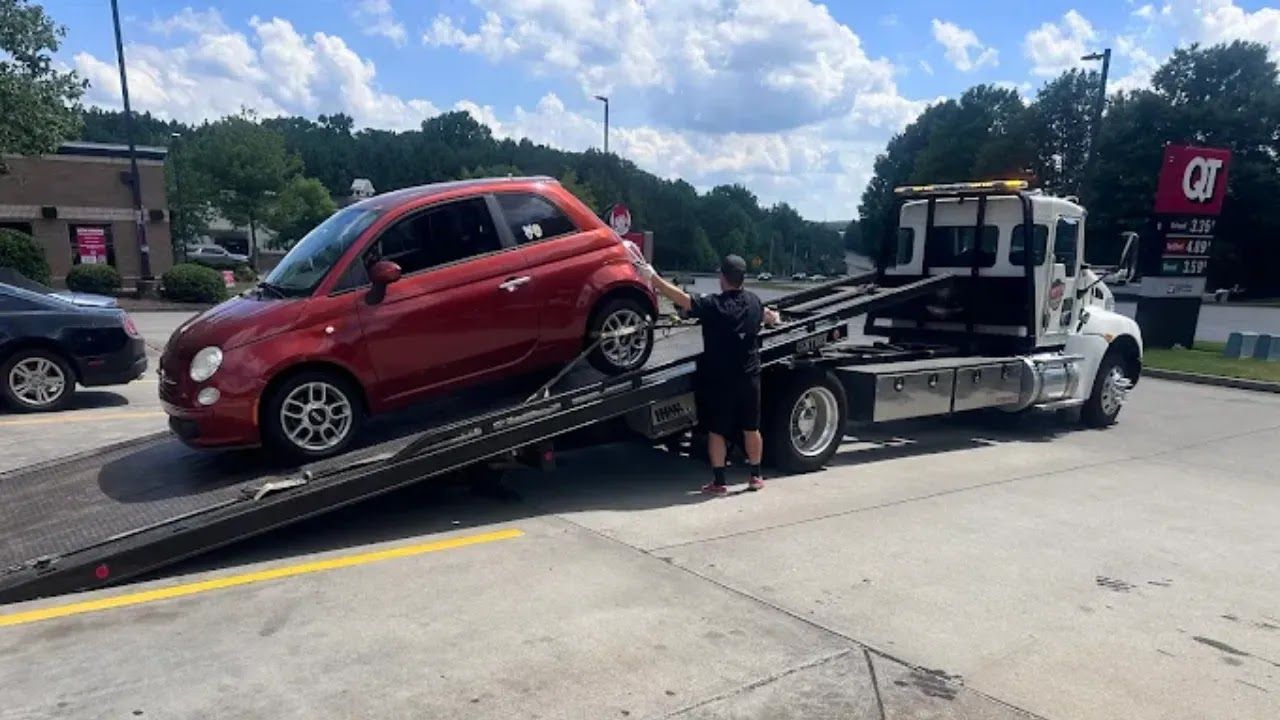 Wrecked red car and white sedan loaded on a tow truck after a crash on a wet roadside
