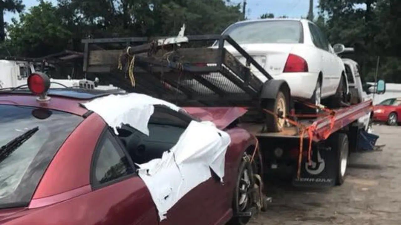 Wrecked red car and white sedan loaded on a tow truck after a crash on a wet roadside