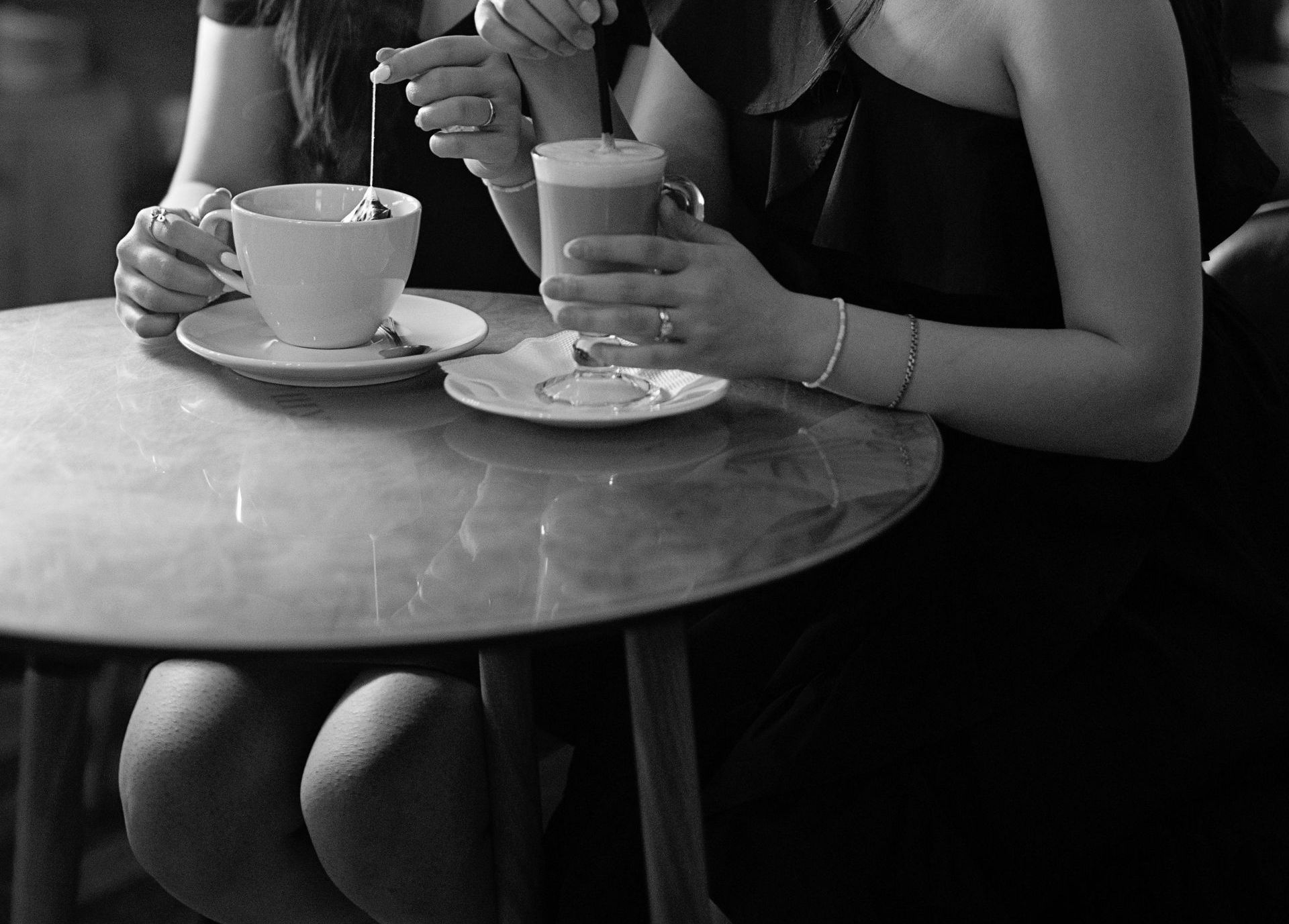zwei Frauen sitzen am Tisch, eine trinkt Tee, die andere einen Latte Macchiato 
