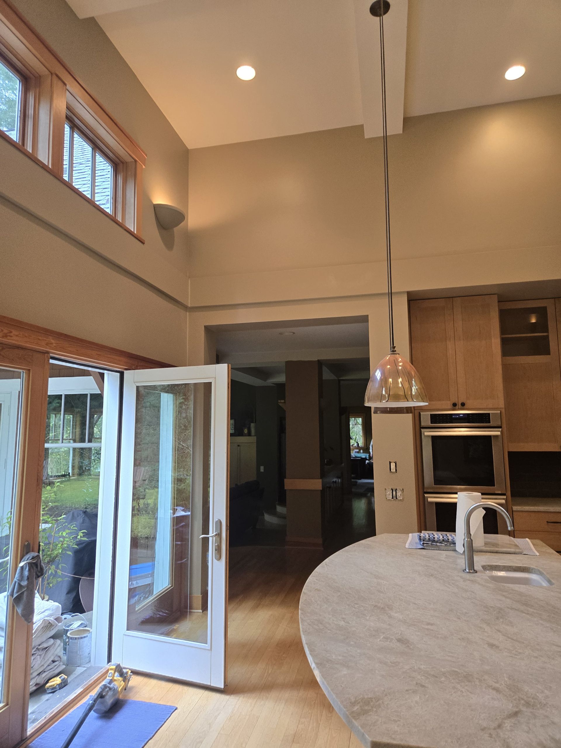 Bright kitchen with open glass doors, large island, pendant light, and tall windows overlooking a yard