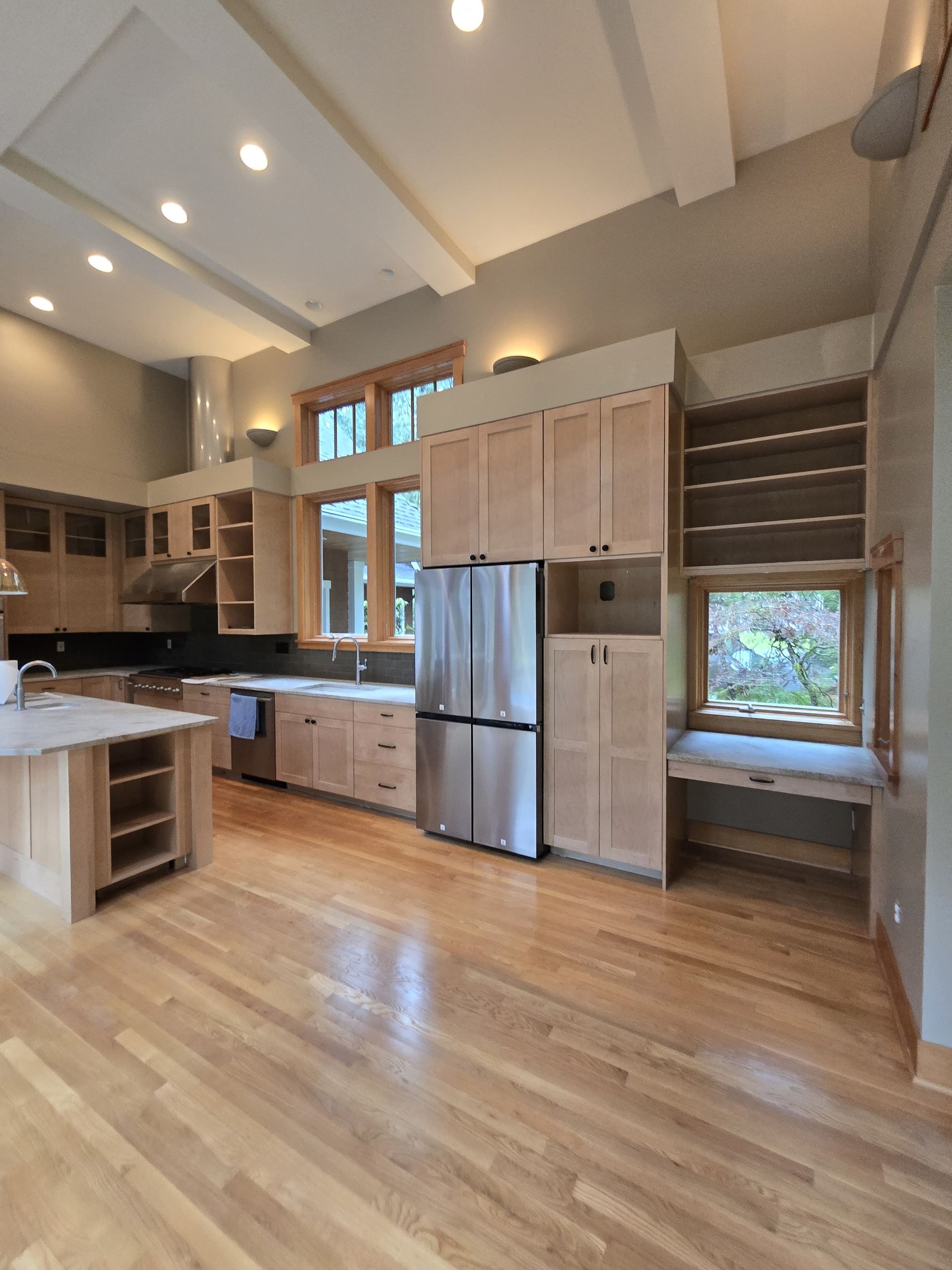 Bright modern kitchen with stainless steel appliances, light wood cabinets, and hardwood floors under high ceilings