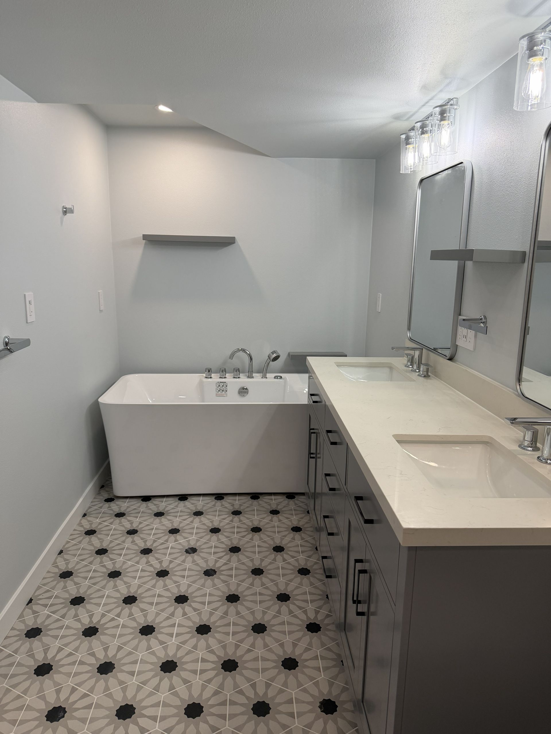 Bright white bathroom with black-patterned tile, vanity, bathtub, and wall mirror.