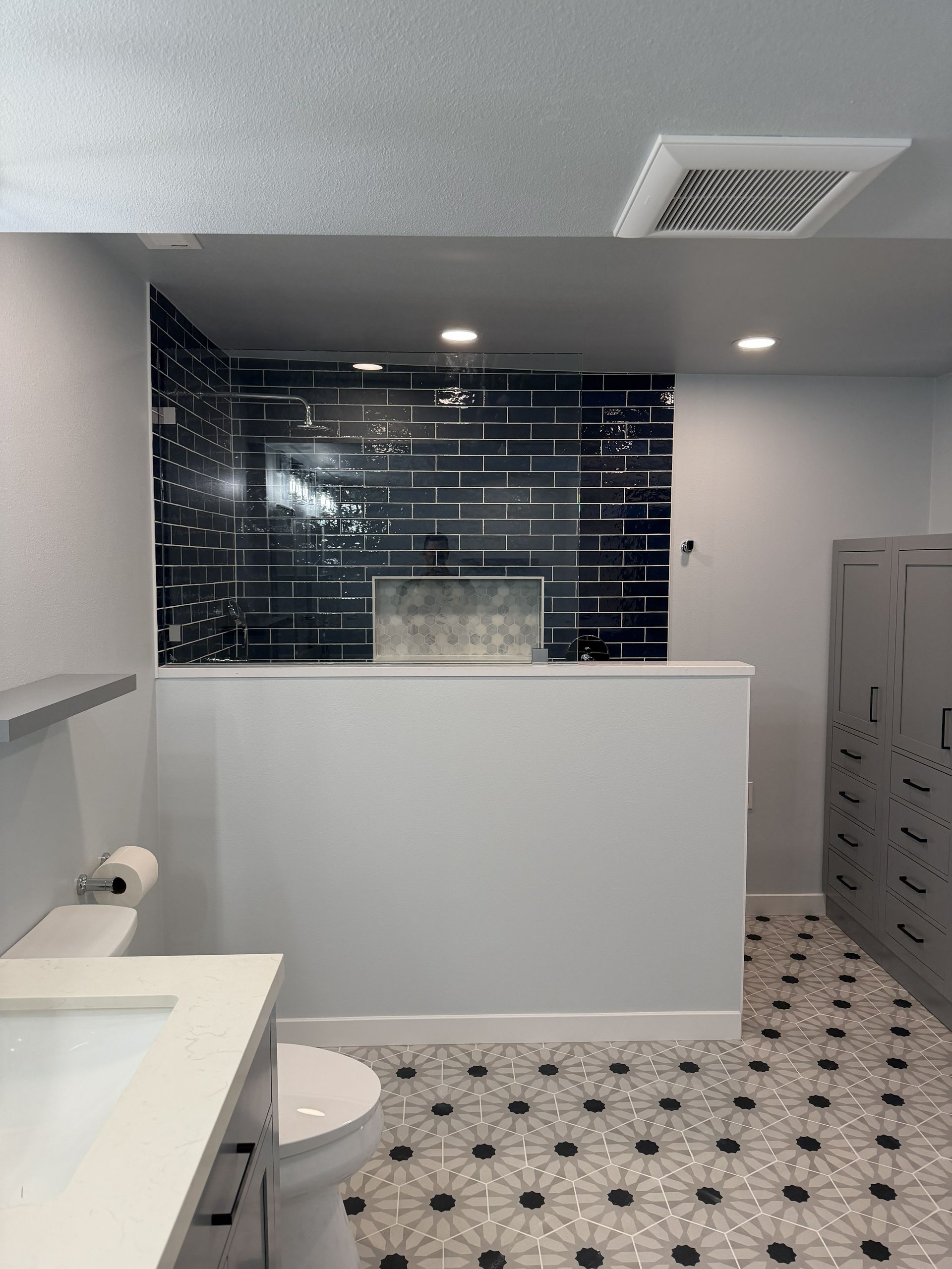 Modern bathroom with white vanity, black tiled shower, and patterned floor tiles