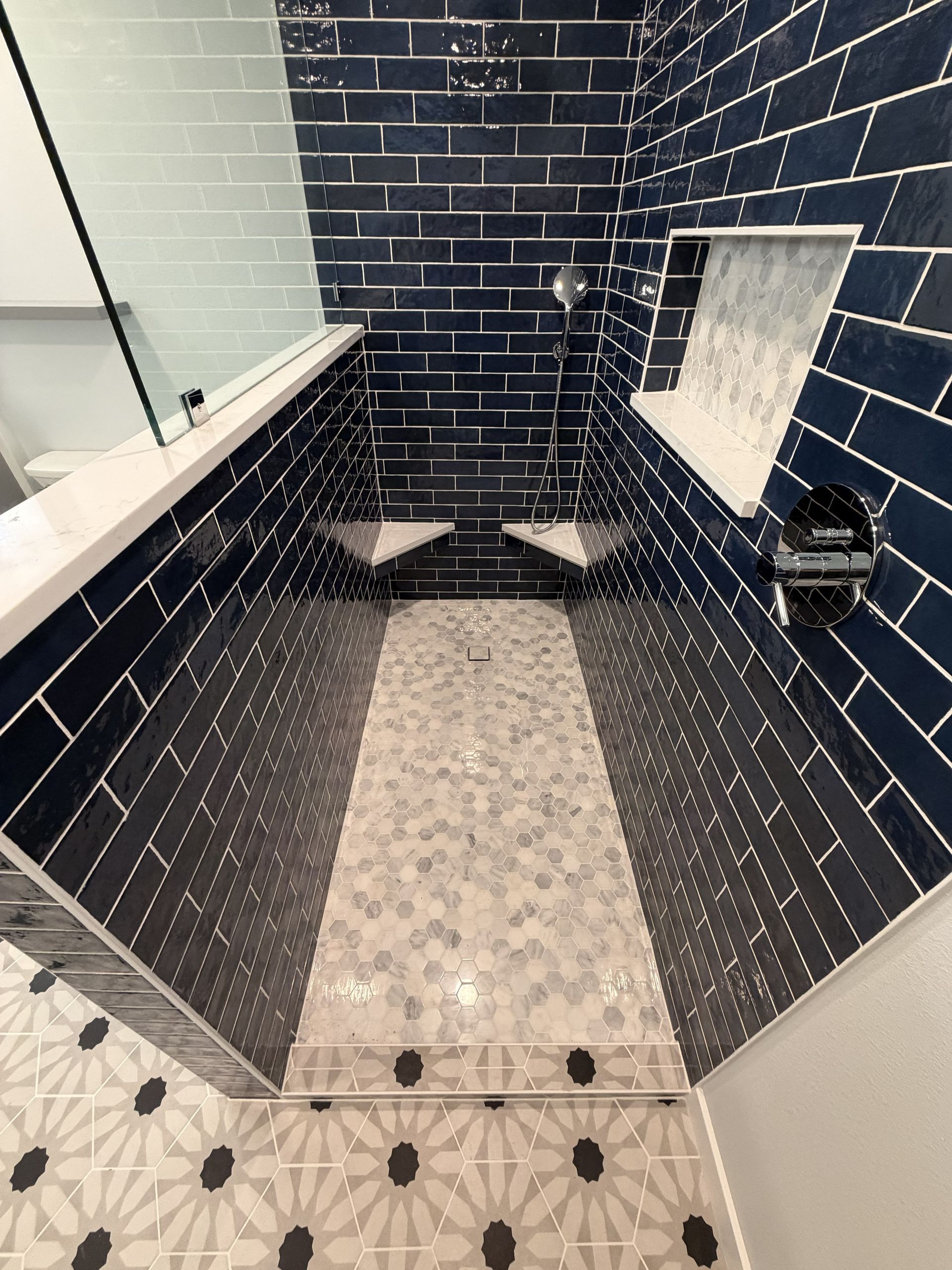 Black-tiled shower stall with white mosaic floor, built-in shelf, and glass partition.