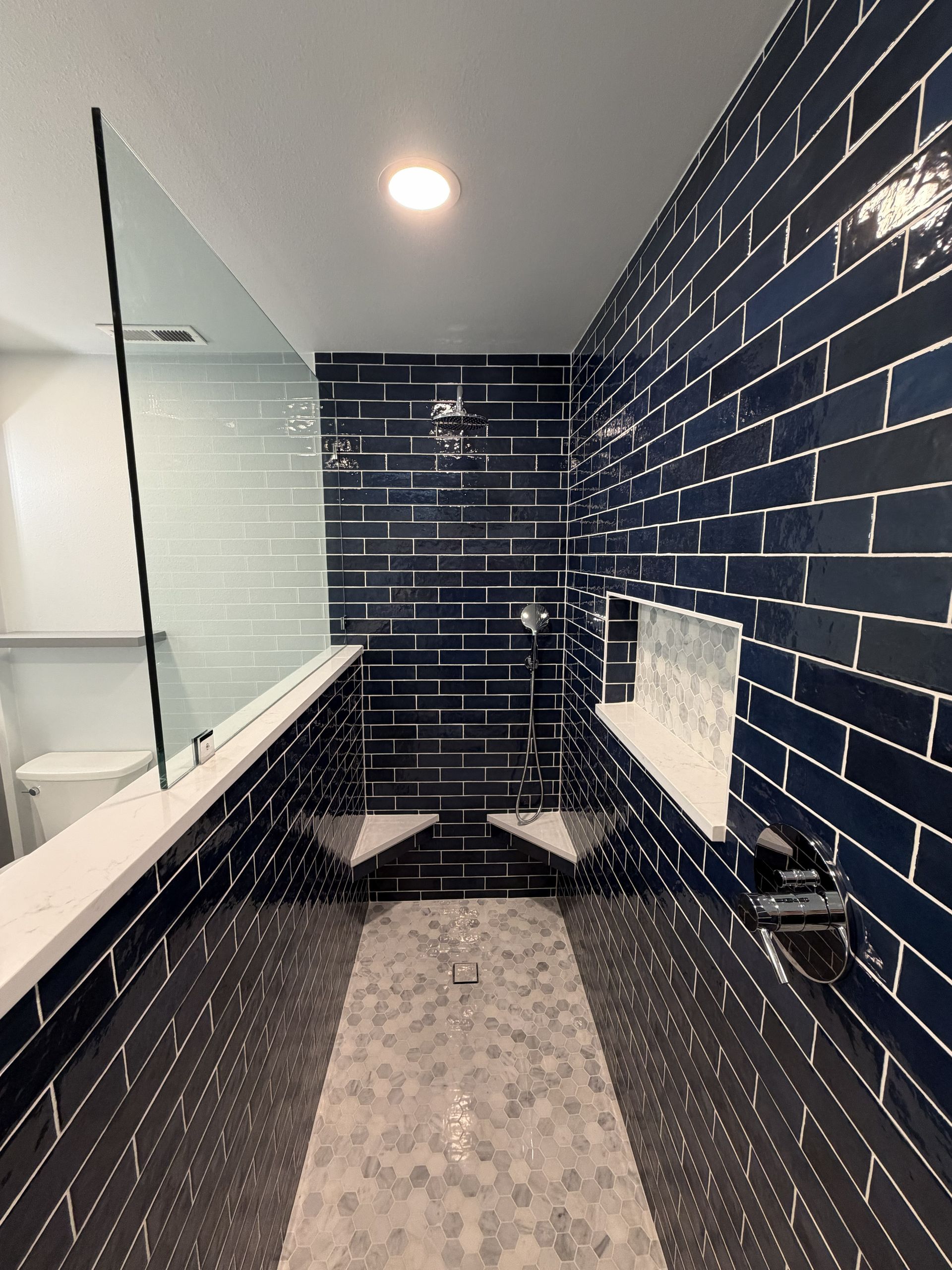 Narrow bathroom with navy subway tile walls, long glass partition, and white sink counter.
