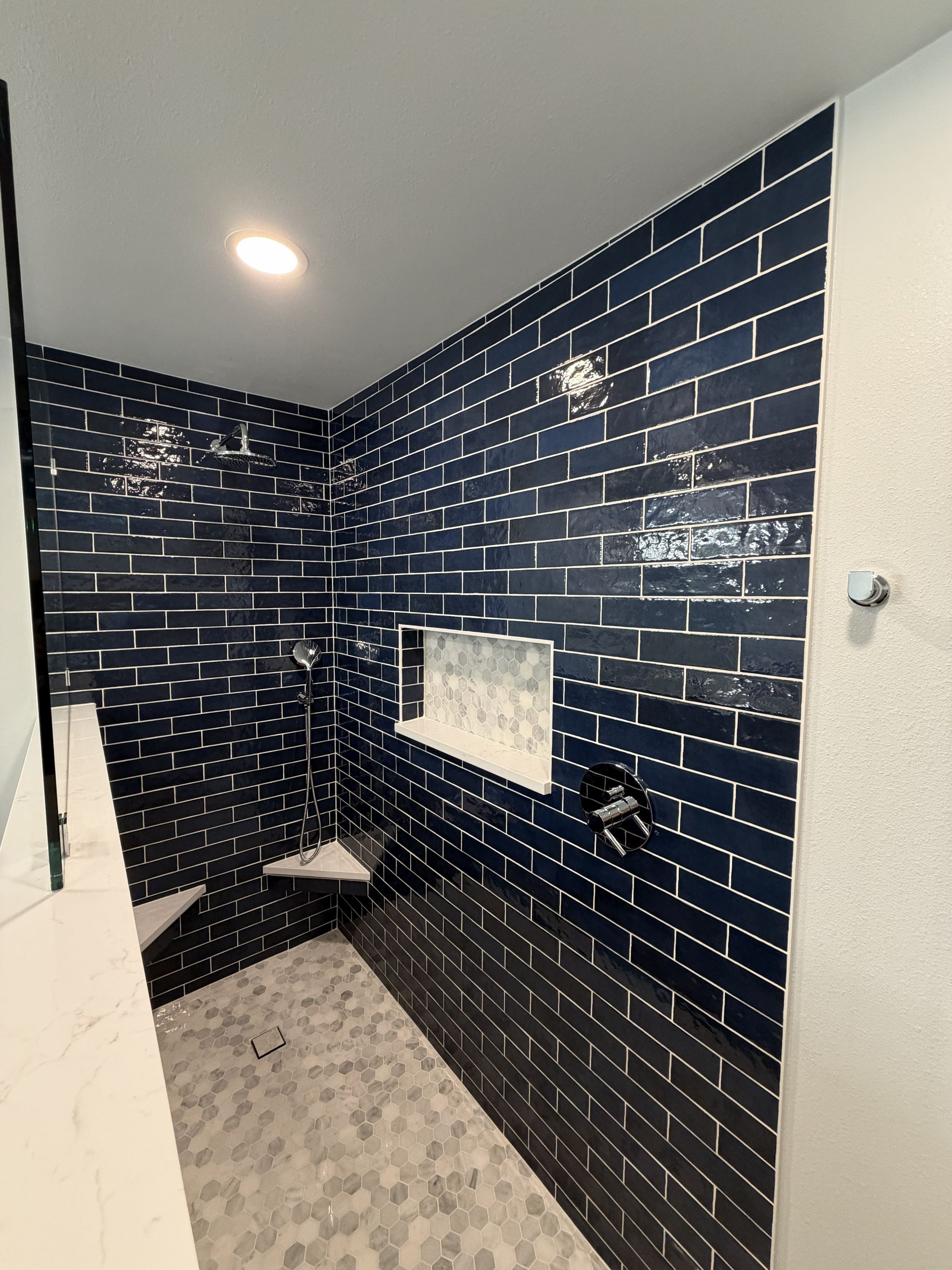 Small tiled shower with dark blue brick walls, white ceiling, and a built-in niche.
