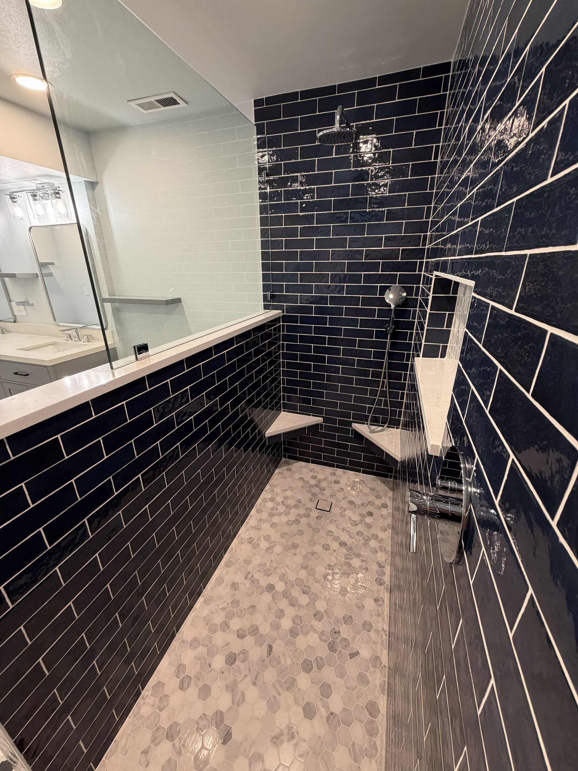 Narrow black-tile bathroom with a long sink, large mirror, and a toilet in the back.