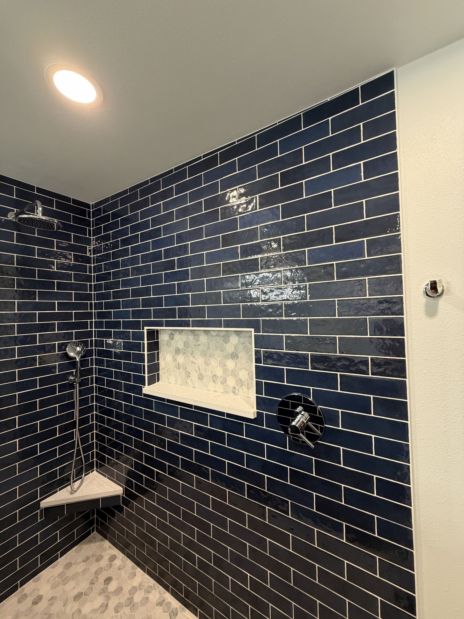 Blue-tiled shower with built-in shelf, corner seat, and shower fixtures.