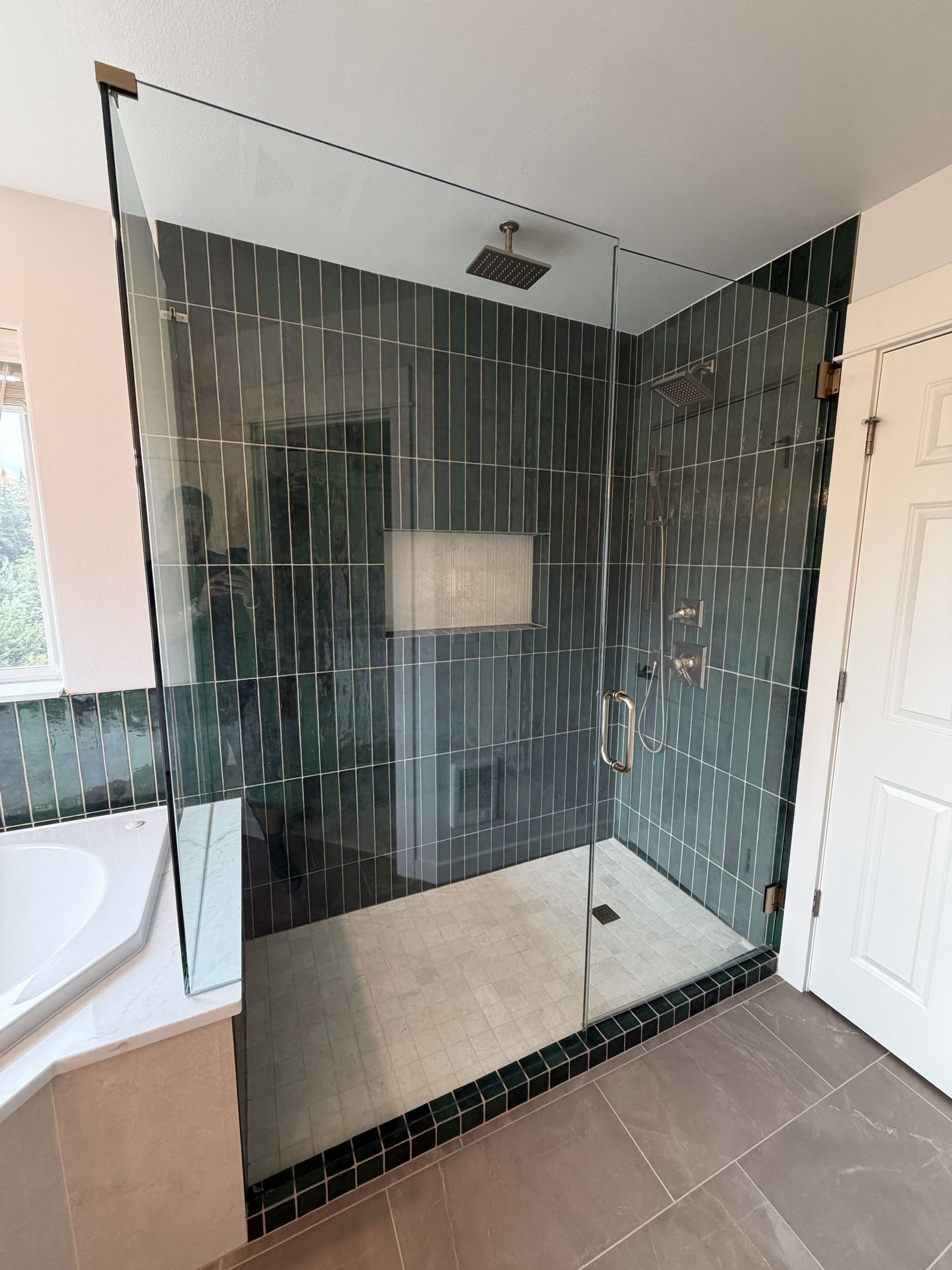 Modern bathroom shower with black framed glass enclosure, dark tile walls, and white door nearby