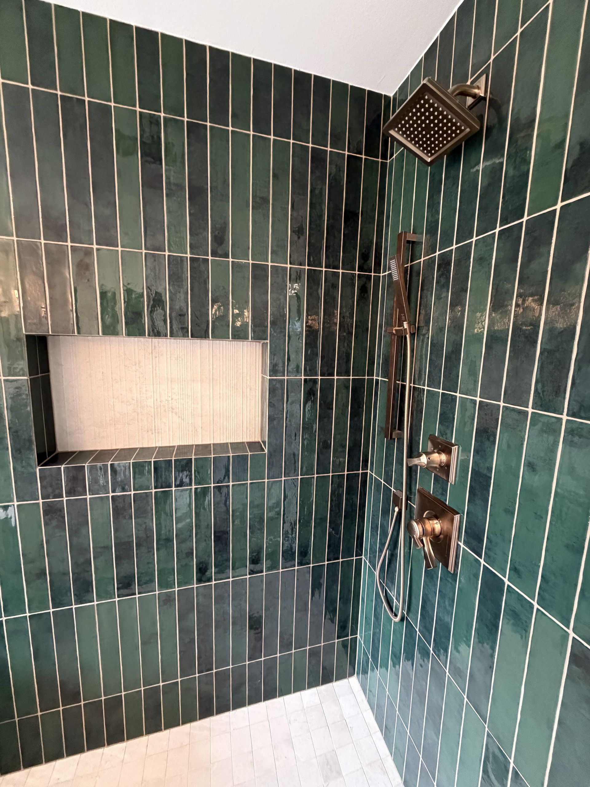 Empty tiled shower with green wall tiles, a built-in niche, and a shower head in the corner.