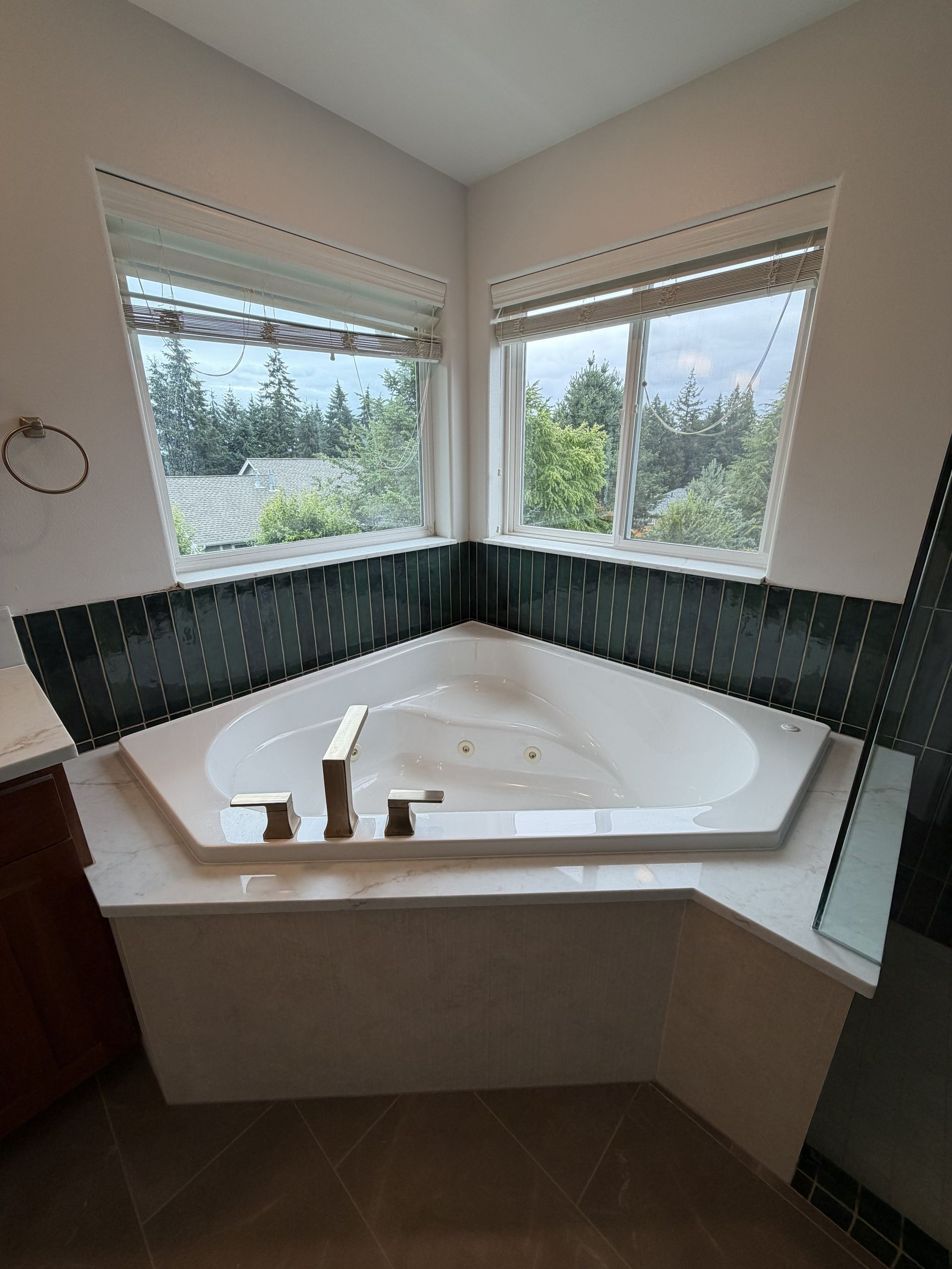 Corner soaking tub with dark tile surround and windows overlooking trees