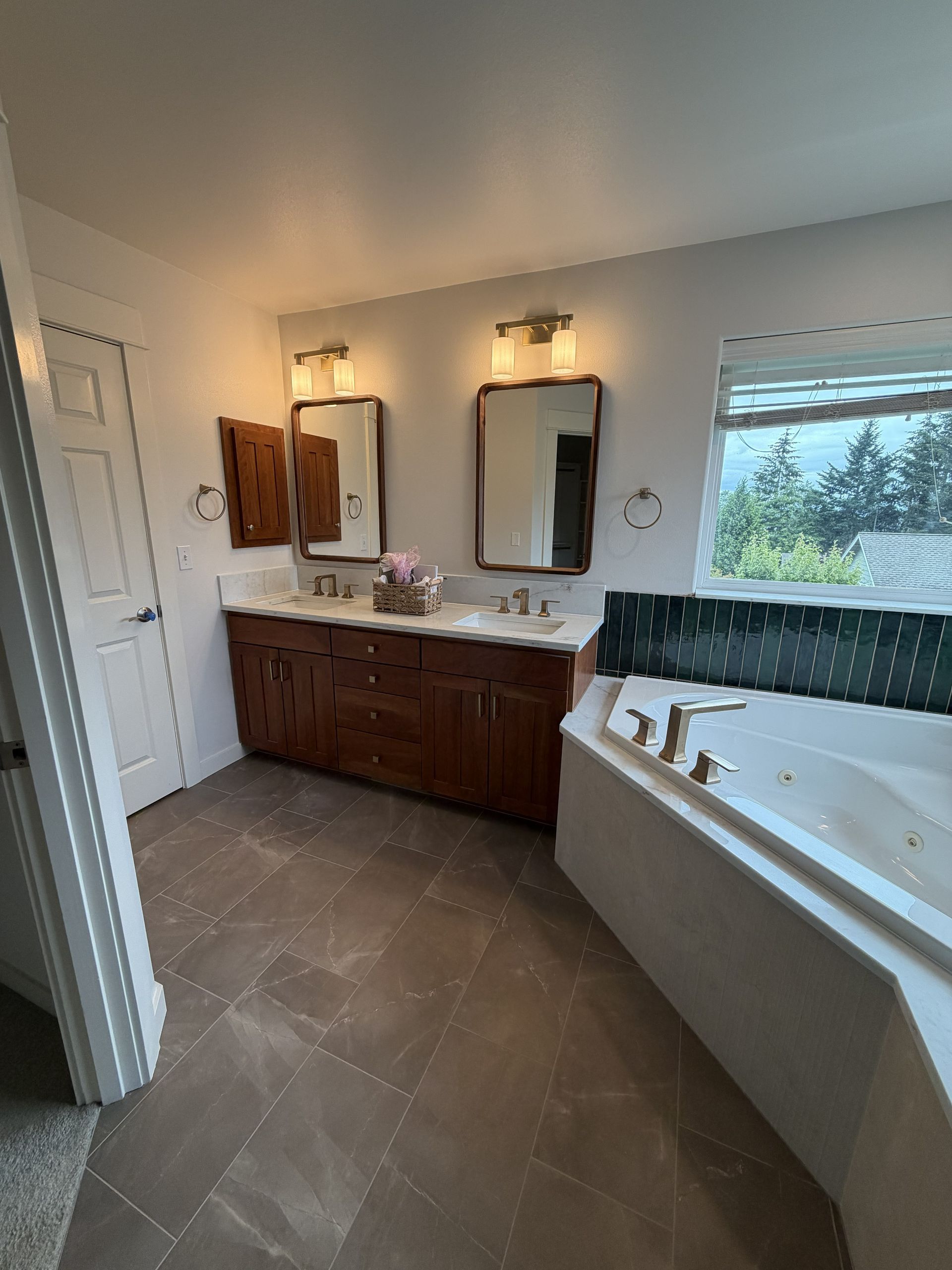Bright bathroom with double vanity, mirrors, and a white soaking tub by a window.