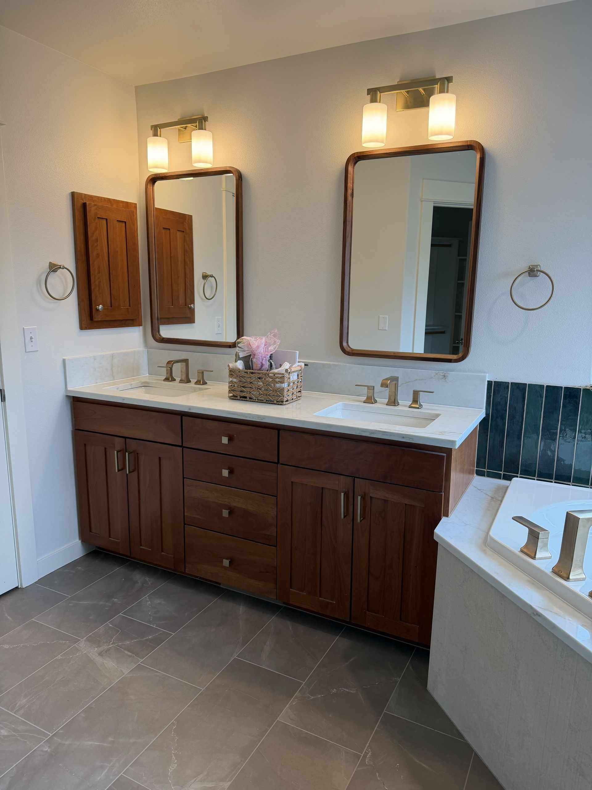 Bathroom with double vanity, wood cabinets, mirrors, wall lights, and a tiled floor.